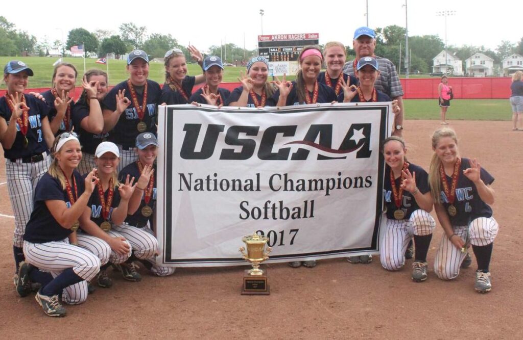 A photo of the SMWC softball team with the National Championship banner and trophy.