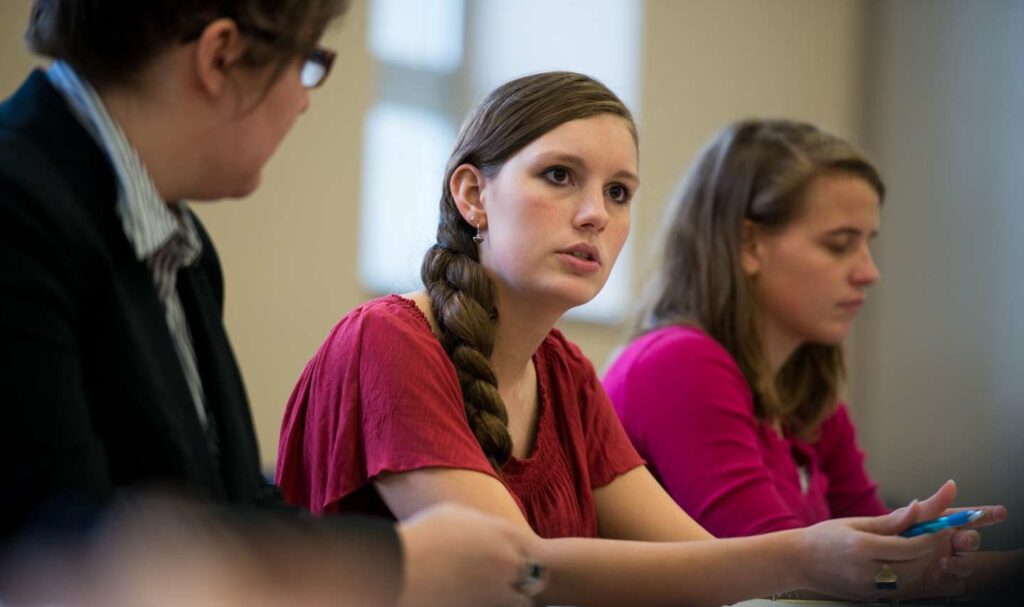 A student in a classroom with an intent face as she shares something with the class.
