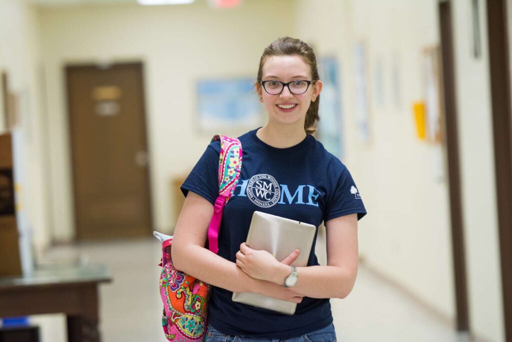 A female student holding her ipad and bookbag smiling.