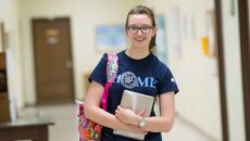 A female student holding her ipad and bookbag smiling.