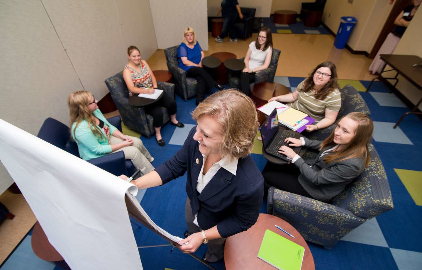 A student writing on a flip chart during a meeting with other students in the Woods Student Center.