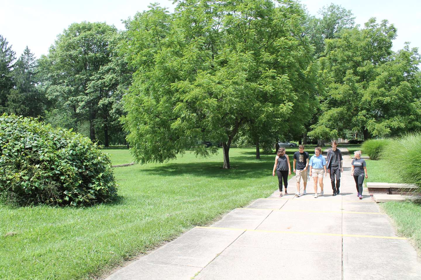 Three female and two male students walk together down the sidewalk in front of Le Fer Hall.