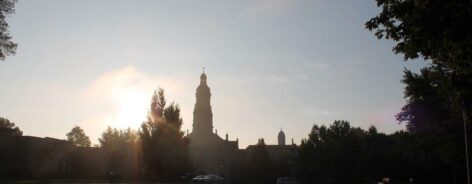The sun rising up over the trees with the silhouette of the Chuch of the Immaculate Conception.