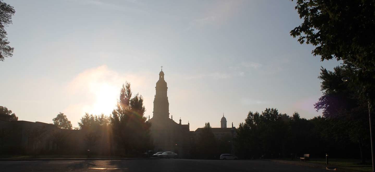 The sun rising up over the trees with the silhouette of the Chuch of the Immaculate Conception.