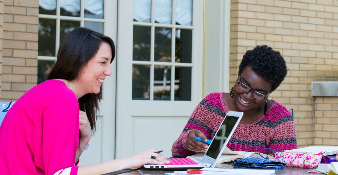 Two students smiling as they study together on the patio outside Le Fer Hall.