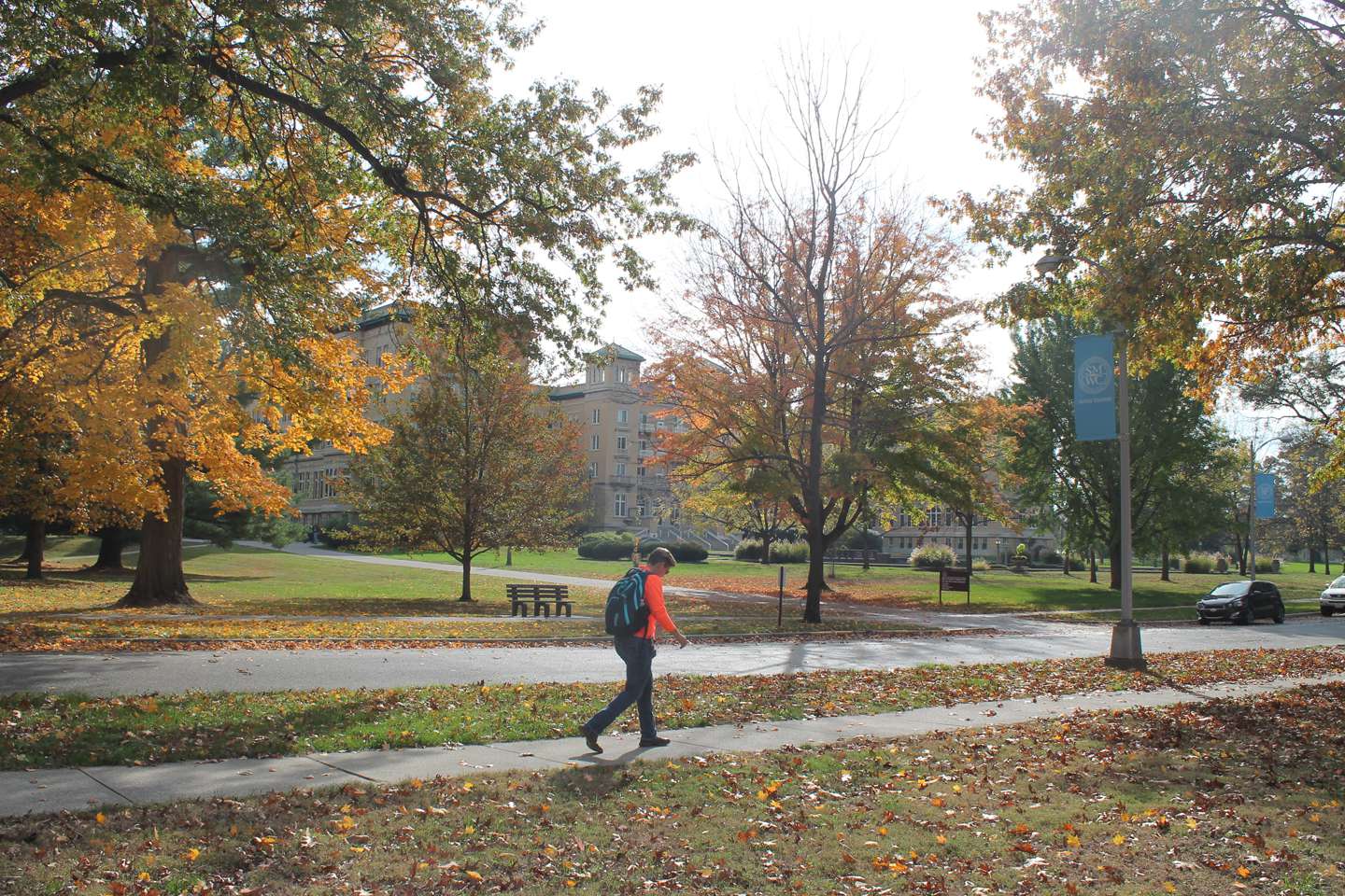 A student walks across campus with the fall leaves and Le Fer Hall in the background.