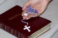 A photo of someone holding a rosary with a Holy Bible.